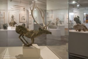 carved caribou in a case with prints visible in the background