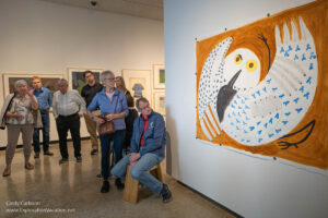 People looking at a large colorful painting of an owl and raven.